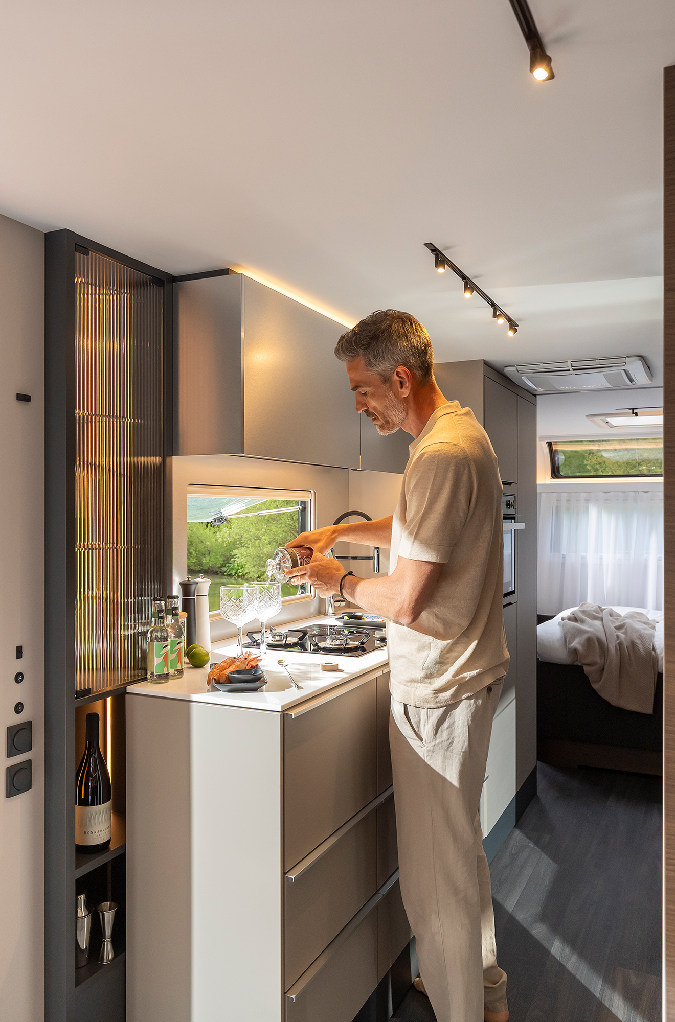 In der Küche des Luxus Wohnwagens ADRIA ASTELLA 754 DP bereitet ein Mann Essen zu.